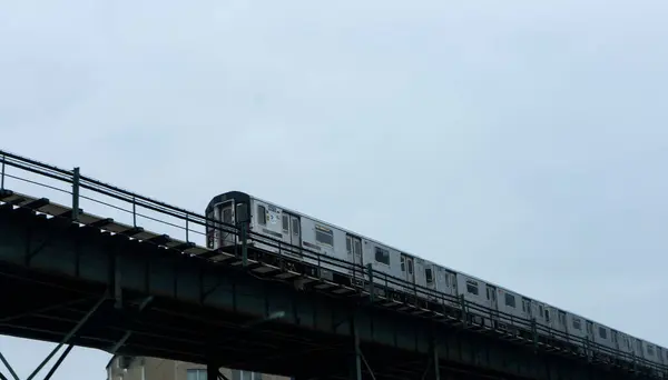 Görüntü, bulutlu bir gökyüzünün arka planına karşı yükseltilmiş bir ray boyunca hareket eden bir treni yakalıyor. Sahne, şehir ulaşımının klasik bir temsili..