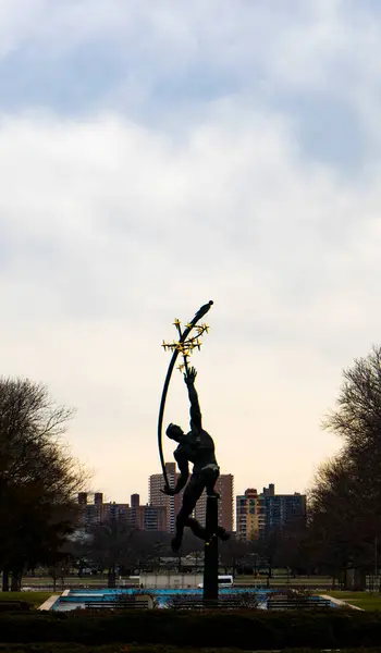 Şehrin siluetine karşı dizilmiş, yıldıza uzanan bir adamın heykeli. Heykel bulutlu gökyüzüne karşı duruyor..