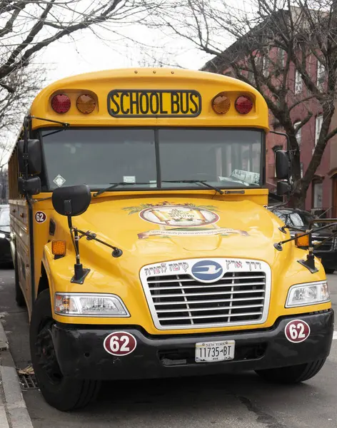 Ön ve yan tarafında 62 numaralı sarı bir okul otobüsü caddenin kenarına park edilmiş. Otobüsün büyük bir ızgarası ve sarı harflerle 
