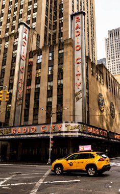 Radio City Music Hall, New York 'ta ünlü bir mekan, önünde sarı bir taksi var. Bina zengin tarihi ve çarpıcı mimarisi ile tanınıyor..