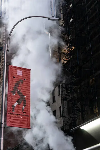 Yerden buharla yükselen bir şehir caddesi manzarası, kısmen kırmızı bir reklam ve bir binanın üzerine metal bir yapı..