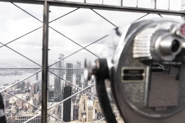 Görüntü, şehrin çarpıcı bir görüntüsünü ön planda madeni para kullanan bir izleyiciyle yüksek bir bakış açısından yakalıyor. Şehir, sayısız gökdelen ve binalarla genişliyor..