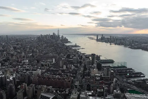 Günbatımında New York şehrinin yoğun ufuk çizgisi ve kıyı şeridini gösteren hava görüntüsünü yakalıyor. Batan güneş bulutlara ve suya ılık bir parıltı saçar..