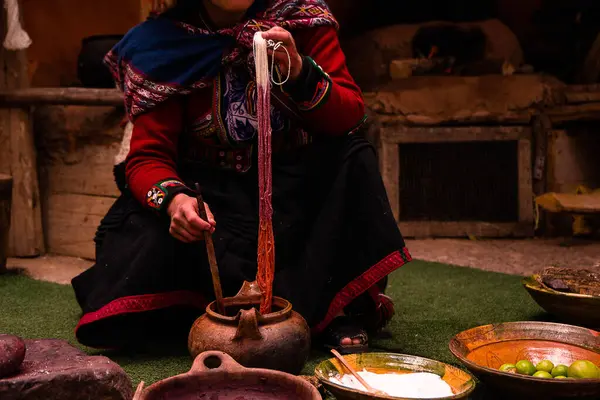 Canlı geleneksel giysiler giymiş bir kadın yerde oturur, etrafında çeşitli kil çömlek ve çatal bıçaklarla yemek hazırlar. Sahne kültürel miras ve basitlik duygusu yayar..