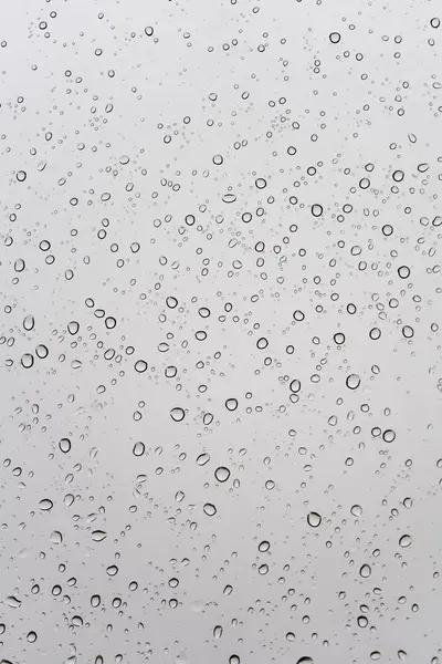 Gri bir yüzeye dağılmış sayısız su damlacıklarının yakın çekim görüntüsü, görsel olarak çarpıcı bir model oluşturur..