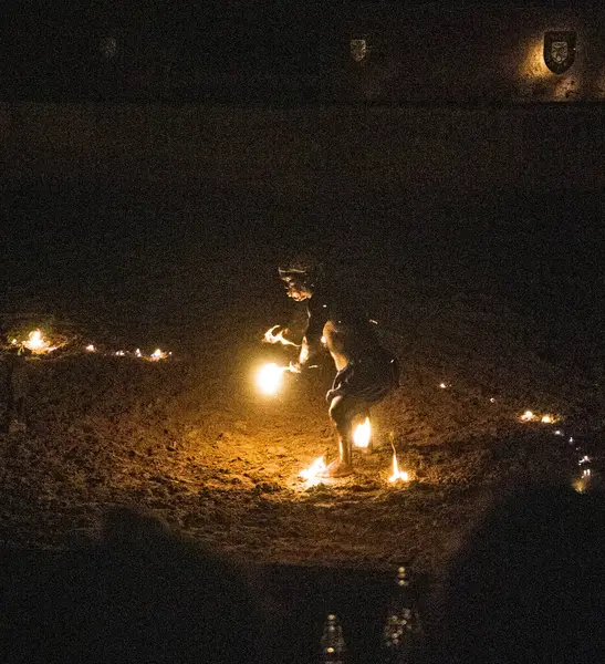 Geceleri ateşle dans eden biri, alevler içinde yerde ve karanlık bir arka planda..