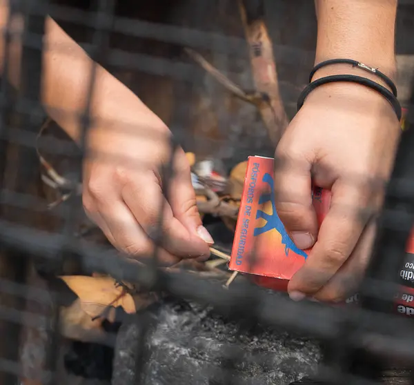 Bir insanın elleri metal bir ızgaranın içinden İspanyol yazıları ve kibrit çöpü olan kırmızı bir kibrit kutusu ile gösterilir..