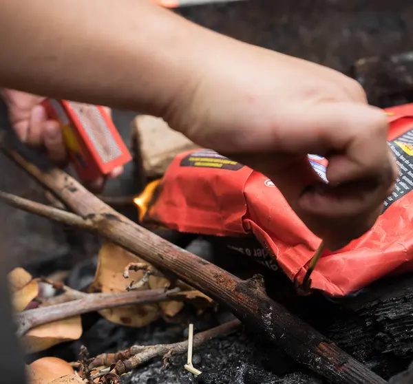 Bir kişi kamp ateşi yakmaya hazırlanıyor, dalları yakmak ve çıra yakmak için dikkatlice kibrit seçiyor. Sahne, açık hava macerası ve kendi kendine yetme anını yakalıyor..