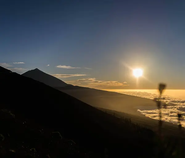 Gün batımında sakin bir dağ manzarası. Altında bulutlar, doğanın sükunetini yakalıyor..