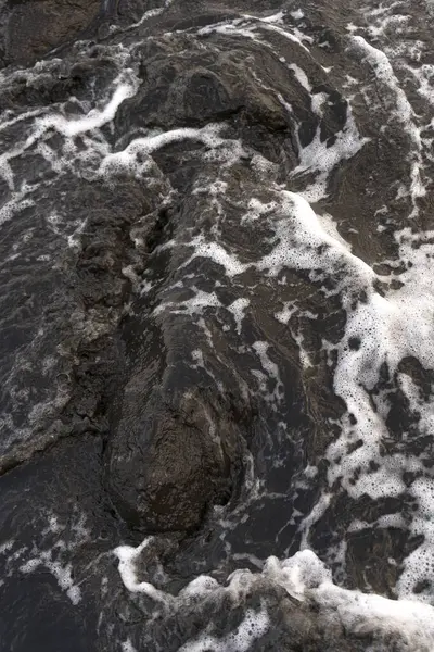 Dalgaların dinamik hareketlerini yakalayan, siyah kayaların üzerinden akan beyaz köpüklü çalkantılı suyun yakın çekim görüntüsü..