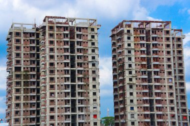 İnşaatın altında beton bloklu veya kırmızı tuğlalı ikiz binalar var. Büyük çok katlı bina, güzel mavi gökyüzü arka planına sahip.