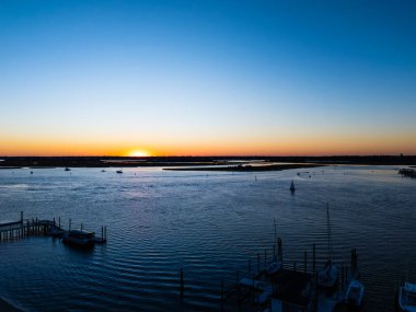 Günbatımına doğru yelken aç. Güneş batarken körfezdeki yelkenli teknelerin hava aracı görüntüsü. Wrightsville plajı NC 'de 60 metrede çekilmiş. Sakin suda birden fazla yelkenli ile çarpıcı bir gün batımı huzurlu bir atmosfer yaratır.