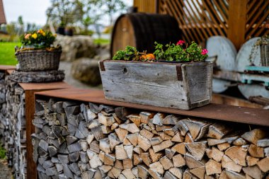 İçinde bir demet çiçek olan ahşap bir sandık bir odun yığını üzerinde oturur. Sandık kütüklerle çevrili. Sahneye kırsal ve doğal bir hava katıyor. Çiçekler renk katıyor.