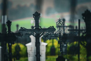 Artistic photo of rapprochement of cast iron crosses at the cemetery in the rain, with a fucked up background of tombstones and greenery