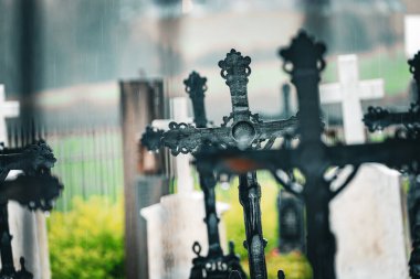 Artistic photo of rapprochement of cast iron crosses at the cemetery in the rain, with a fucked up background of tombstones and greenery
