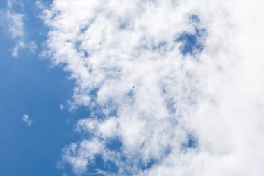 Parçalı bulutlu gökyüzünde uçan küçük bir dron, beyaz bulutlar ve mavi gökyüzü arkaplanı ile minimalist bir kompozisyon. Teknoloji, gözetleme, hava fotoğrafçılığı veya özgürlük gibi konular için mükemmel..