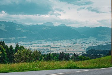 Bulutlu bir gökyüzünün altında köyleri, tarlaları ve ormanlı tepeleri olan bir İsviçre Vadisi 'nin huzurlu panoramik manzarası. İsviçre 'de bir yol kenarında yakalandı..