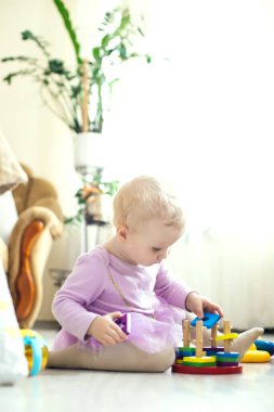 Kız oturma odasında oyuncak oynuyor. Montessori tahta oyuncağı katlanmış piramit. Çember, dörtgen, üçgen, çocuk oyuncaklarının tahta unsurlarını dikdörtgen yap. Çok renkli oyuncak mavi, sarı, kırmızı, yeşil.