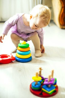 Kız güneşli bir günde oturma odasında yerde mantıksal piramit oynuyor. Montessori tahta oyuncağı katlanmış piramit. Çember, dörtgen, üçgen, çocuk oyuncaklarının tahta unsurlarını dikdörtgen yap. Çok renkli oyuncak mavi, sarı, kırmızı, yeşil