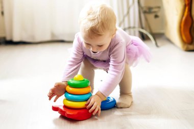 Kız güneşli bir günde oturma odasında yerde mantıksal piramit oynuyor. Montessori tahta oyuncağı katlanmış piramit. Çember, dörtgen, üçgen, çocuk oyuncaklarının tahta unsurlarını dikdörtgen yap. Çok renkli oyuncak mavi, sarı, kırmızı, yeşil