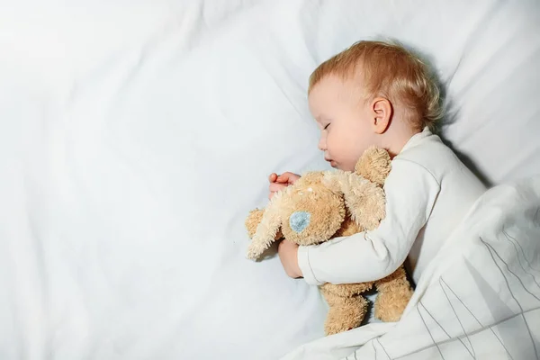 sweet little girl sleeps on white linen in bed. child 1 year old sleeps hugging soft toy. Happy childhood and sleep problems in children concept