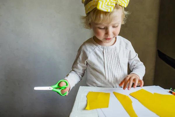 Little blonde girl with scissor at preschool. Portrait of a little Cute baby girl cutting a paper