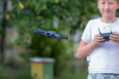Uzaktan kumandalı bir ergen. Çocuk evin bahçesindeki oyuncak bir dronu kontrol ediyor..