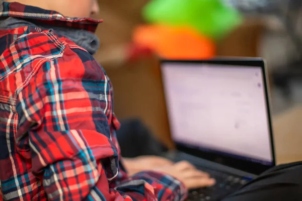 stock image boy in plaid shirt does lessons on laptop. child learns remotely during quarantine of coronavirus. Online learning from home.