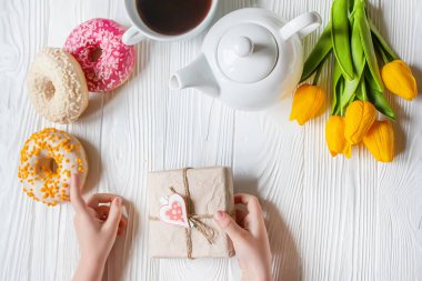 Çocuğun elleri bir buket lale ve donut tutuyor. Sevdiğin için yatakta romantik bir sevgililer günü kahvaltısı. Anneler Günü, 8 Mart. Düz yatıyordu. Üst görünüm