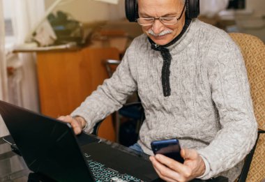 Evde dizüstü bilgisayarda çalışan kıdemli bir adam. Evde dizüstü bilgisayarda çalışan kıdemli bir adam. Yaşlı adam kredi kartı numarasını telefona kaydediyor. Emekliler için krediler