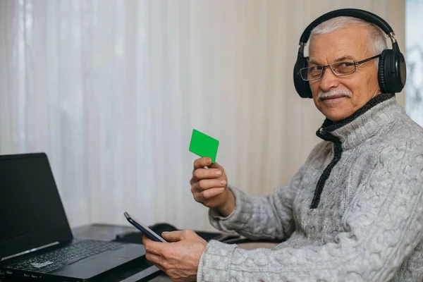 Senior man working at laptop at home. Old man enters credit card number into phone. Loans for pensioners. Opening retirement accounts. elderly man shows credit card. mockup. Clipping path