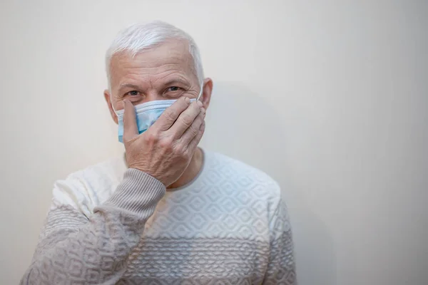 Elderly man in protective medical mask isolate in white. Coronavirus elderly advice. Safety old men. Copy space. man touches face with hand. Mistakes in wearing protective masks. Transmission of virus through touch.