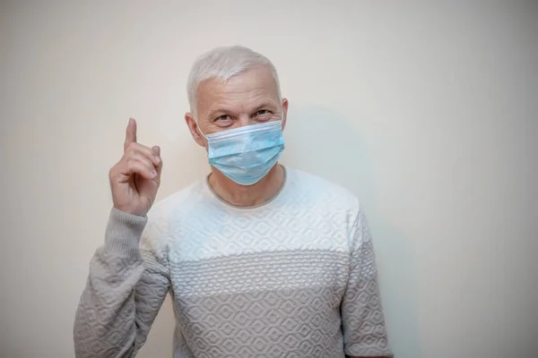 elderly handsome man in medical mask raised finger to top. pensioner in protective mask advises to protect against viruses, coronavirus, influenza.