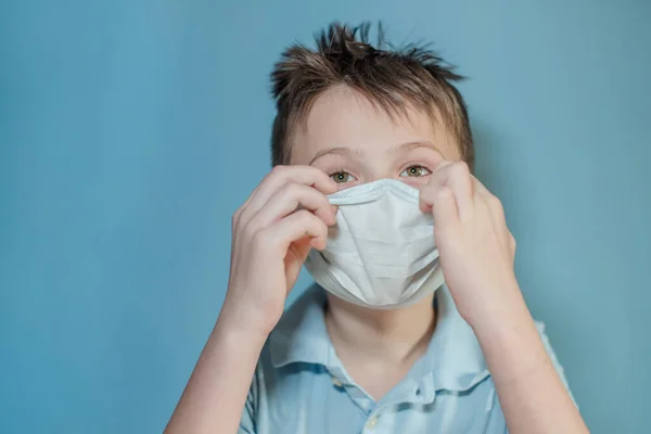 Stock image boy adjusts protective medical mask on face. Mistakes in dressing the mask. child touches face and carries virus. child with influenza or cold protected from viruses among patients with coronavirus