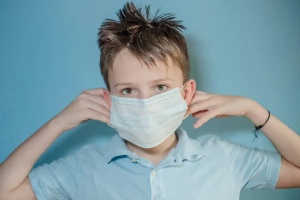 boy wears protective medical mask on face. child tucks the gum behind ears from mask. child with flu, influenza or cold protected from viruses among patients with coronavirus.