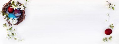 Paskalya yumurtaları ve beyaz ahşap arka planda çiçek açan kiraz dallarıyla dolu bir yuva. Doğal boyalarla boyanmış çavdar yumurtaları. Bahar dini tatil konsepti. Boşluğu kopyala