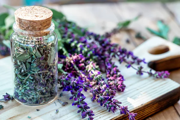 stock image Dry purple sage flowers in a glass jar with a cortical lid. A sage plant on a wooden cutting board. preparation of medicinal herbs drying