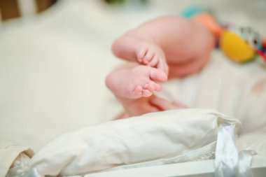Yeni doğmuş bir bebeğin bacakları. Beyaz çarşafla beşikte sürünmeyi öğrenen bebek pembe bacakları. Tanınmayan küçük bir kız beşiğinde taşınıyor. Odaklanmamış