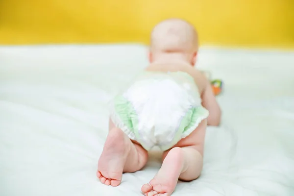 Rear view of a child crawling in a pump. Infant hygiene. Protection against the flow of urine for newborns. Child care. Cute baby on a white sheet and against a yellow wall. Defocused