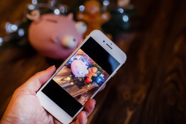 Noel 'de telefonda domuzcuk kumbarası ve fenerli bir çelenkle çekim yapmak. Akıllı telefonu tutan bir el. Telefonunda fotoğraf çekmeyi öğrenmek.