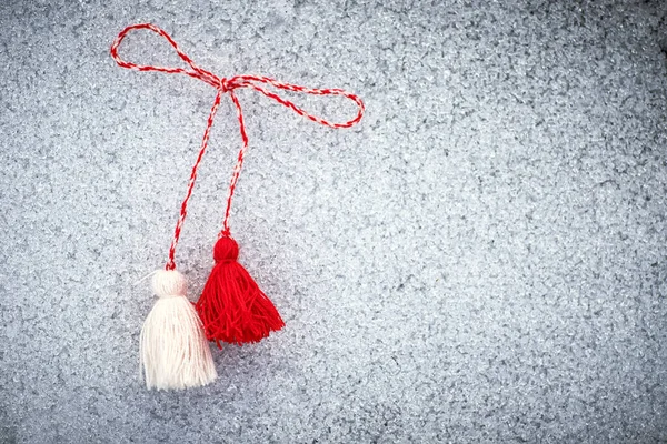 stock image martenitsa. Bulgarian Symbols of spring. Red and white tassels of threads on the ground covered with snow. Baba Marta Day. Wallpaper of spring flowers.