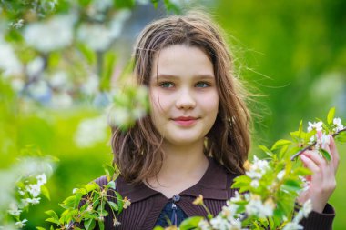 Baharda kiraz çiçeklerinin arasında güzel bir kız. Kahverengi saçlı ve yeşil gözlü bir kızın portresi..