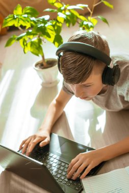 Çocuk ders veriyor. Dizüstü bilgisayarın yanında ders kitabı ve yerde ödev için bir not defteri var. Uzaktan yakından takip edilen gölgelerle birlikte Coronavirus karantinasını öğreniyor..