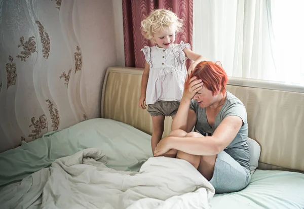 stock image happy girl stands near unfortunate mother. tired mother covered eyes with hand. Difficulties of raising children up to 3 years. Stop hysteria