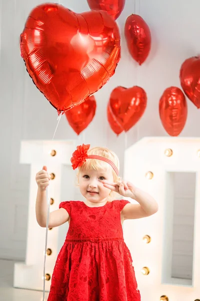 little girl shows two fingers and holds Red heart balloons. Valentine\'s Day Concept. big letters LOVE.