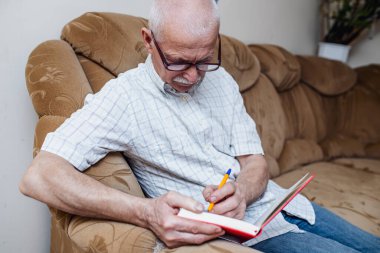 Yaşlı adam kanepede otururken planör ya da deftere notlar alır. Emekli adam serbest çalışıyor, kariyeri bittikten sonra iş yapıyor.