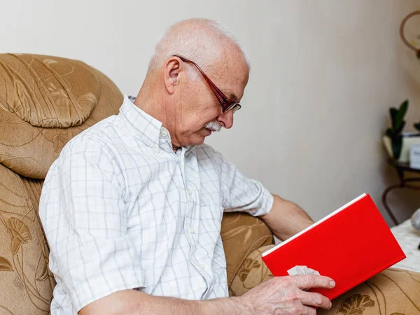 Senior man reading book at home. An elderly businessman makes a business plan sitting at home in a room on the couch. Organization of business by people for 65 years