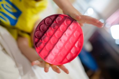 Viva Magenta tonu yeni yürümeye başlayan çocuğun eline geçti. Çocuk elinde tutuyor, patlat. Yatakta stres önleyici bir oyuncakla neşeli bir çocuk. Baloncuklu yumuşak oyuncaklar. Çocuk gökkuşağı pop-it ile oynuyor. Renk 2023