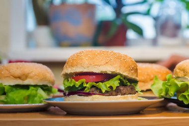 Üç ev yapımı hamburger, domates ve köfte, akşam yemeği için mutfak masasında taze tahıllı çörek.