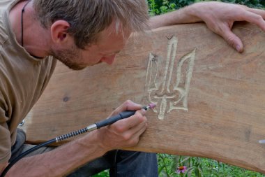 Adam uzun süre çalıştı. Adam bankta Ukrayna armasını kesiyor. Adam bir süsü kesici ile keser - matkap başlığı